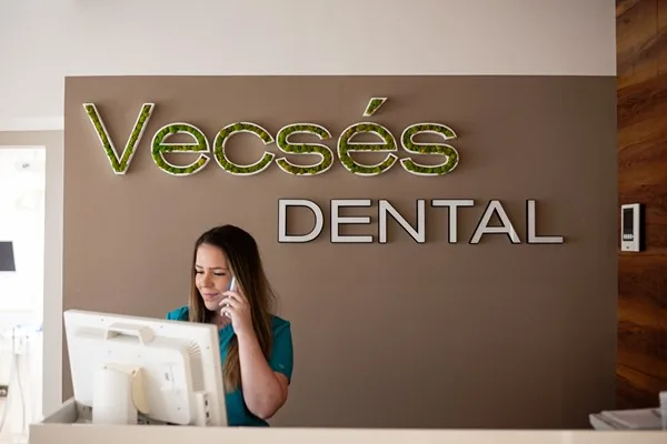 Recepciósunk telefonon egyeztet időpontot a Vecsés Dental fényreklámja előtt